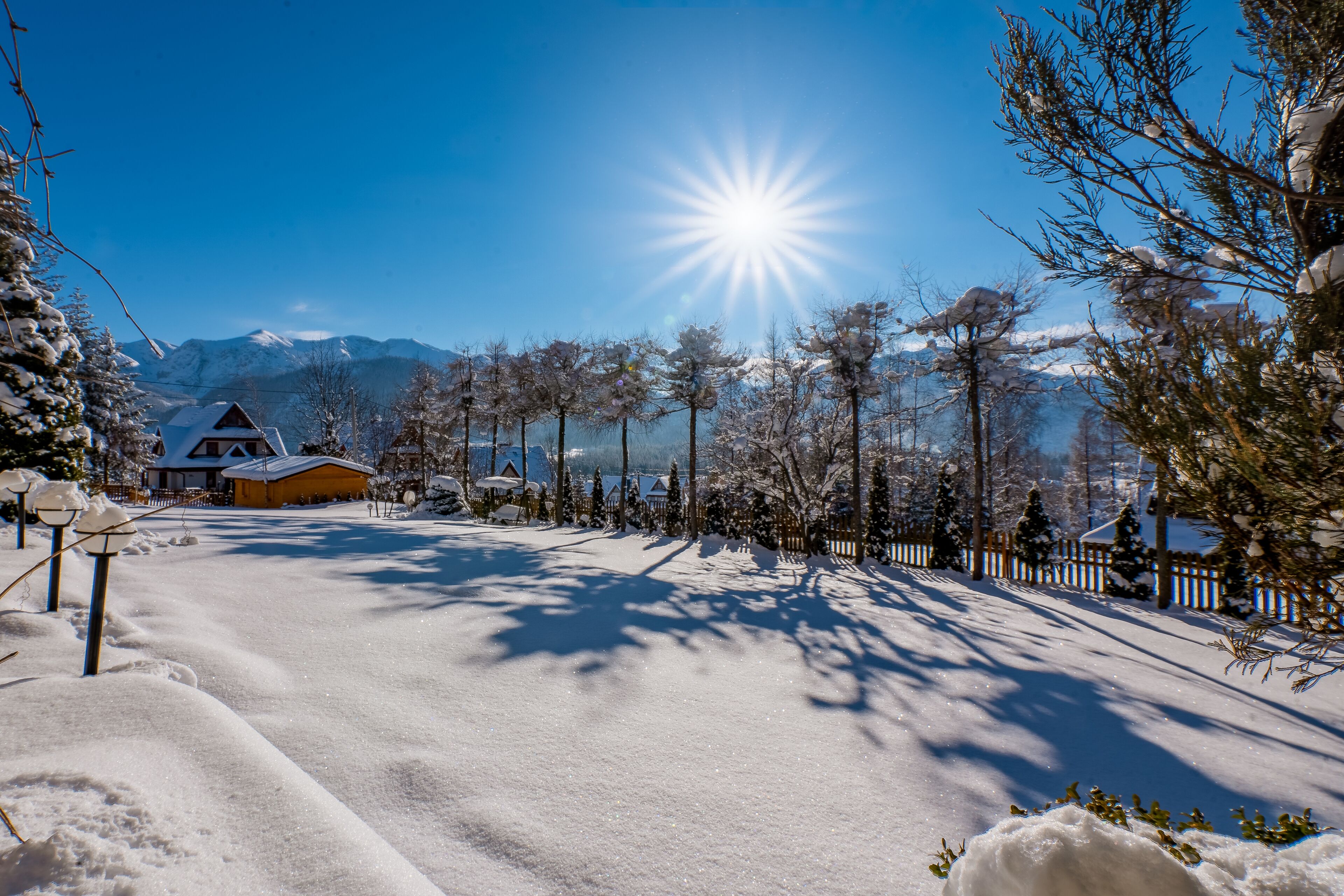 A snow-covered landscape with a house, trees, and mountains in the background.
