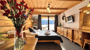 Uma cabana de madeira com uma cama, uma mesa de jantar com um vaso de flores, uma televisão e vista para as montanhas.