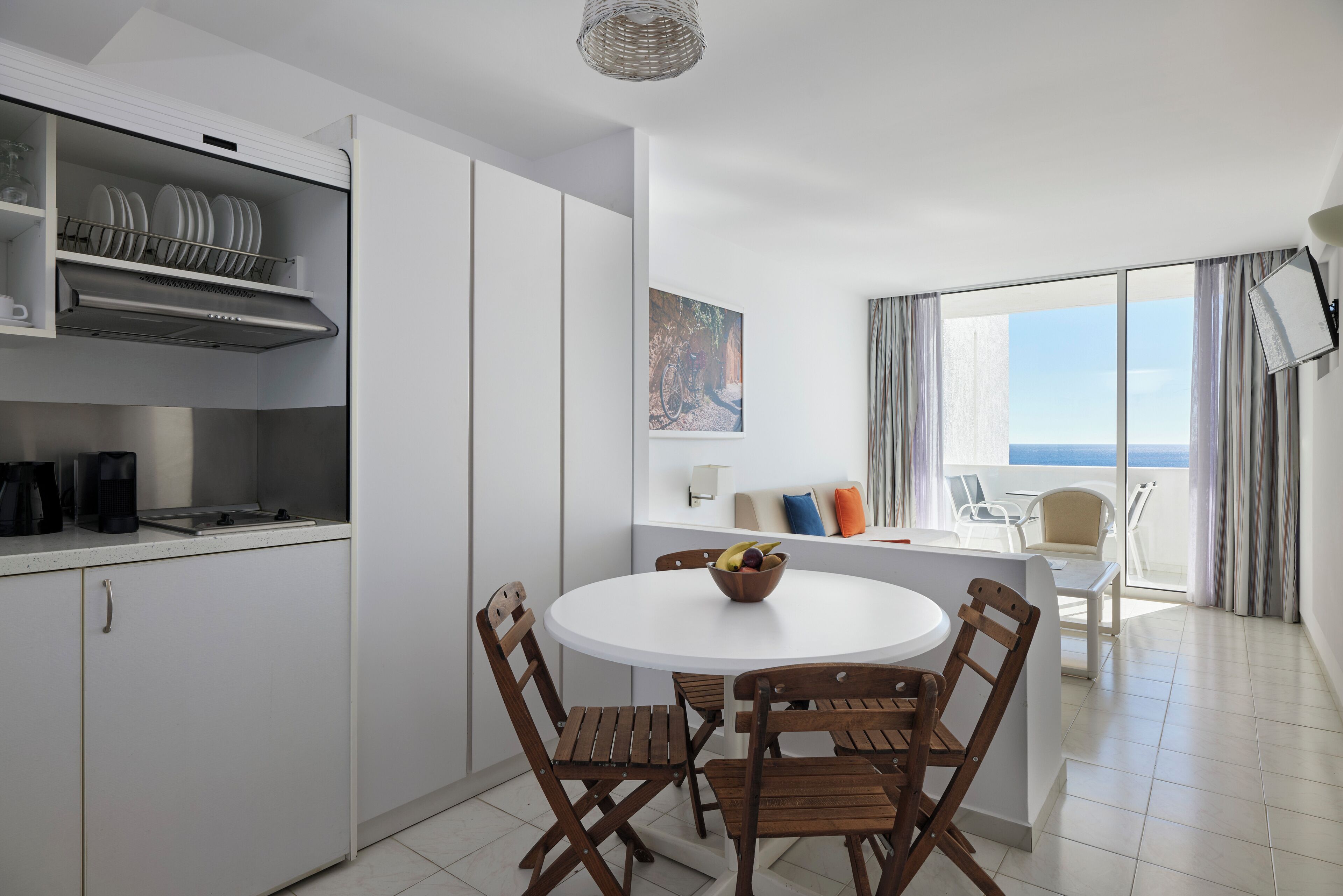 Une cuisine moderne avec des meubles blancs, un coin repas avec des chaises en bois, une table ronde et un balcon avec vue.