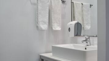 Un baño moderno con un lavamanos blanco, un espejo y dos toallas colgadas en un perchero.