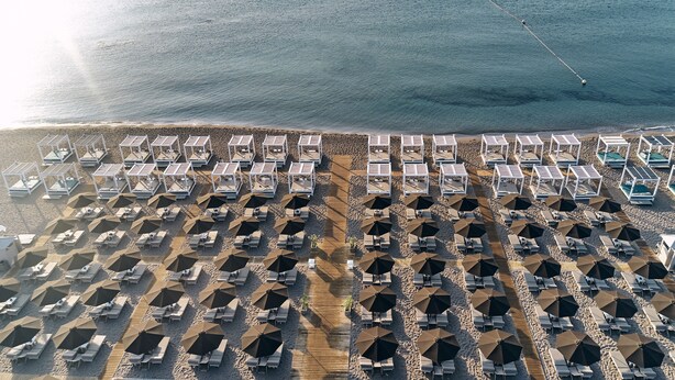 An aerial view of a beach with rows of sunbeds and umbrellas, a wooden walkway, and a clear view of the sea. - Epsilon Hotel Apartments (Rhodes)