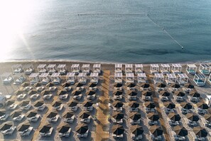 An aerial view of a beach with rows of sunbeds and umbrellas, a wooden walkway, and a clear view of the sea. - Epsilon Hotel Apartments (Rhodes)