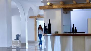 A spacious lobby with a polished tile floor, a reception desk with wooden beams, and a seating area with a striped chair.