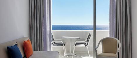 A hotel room with a balcony, a sofa with cushions, two chairs, and a table.