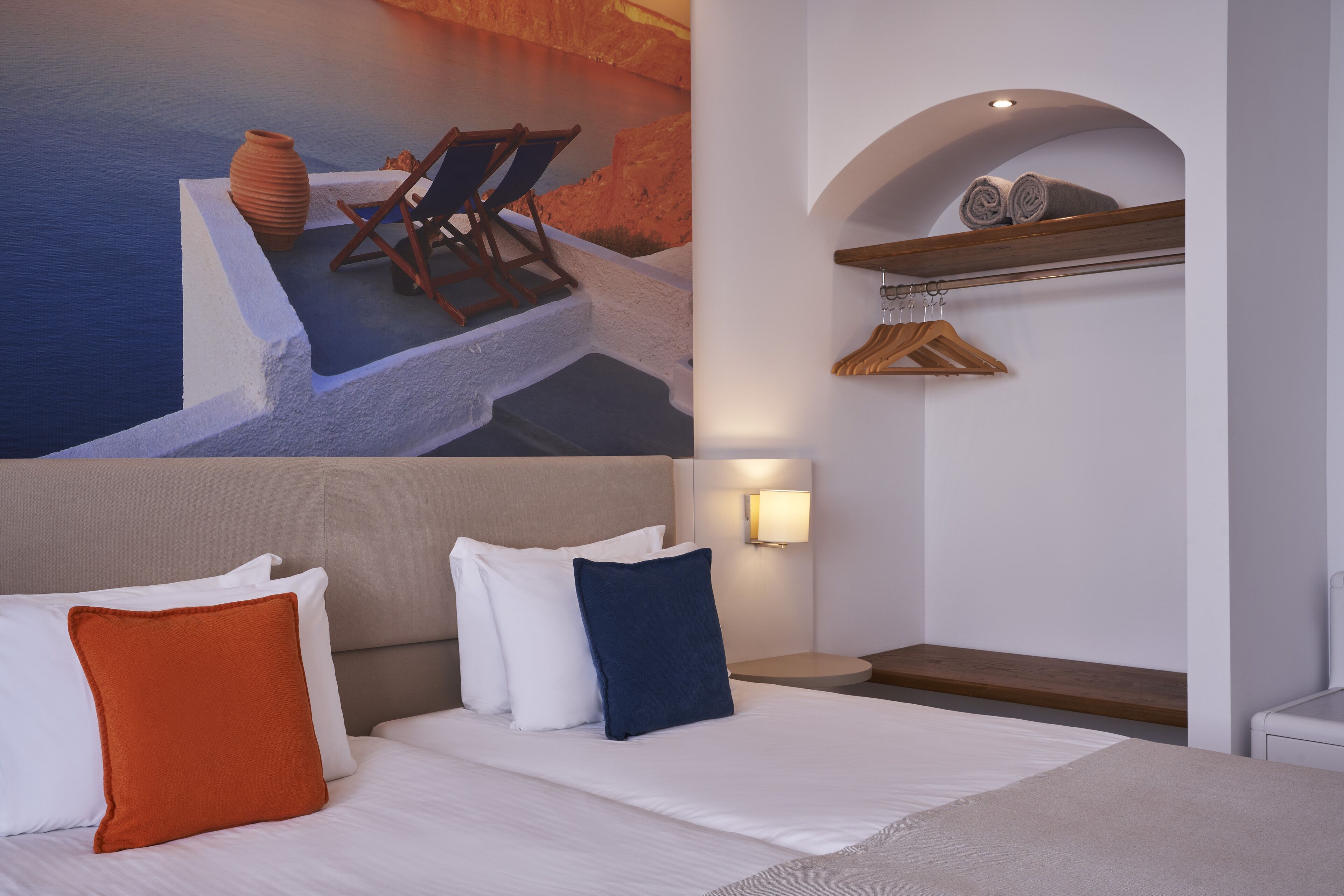 Habitació d'hotel amb un llit, una tauleta de nit, un portaToalles fixat a la paret i un mural d'una escena costanera.