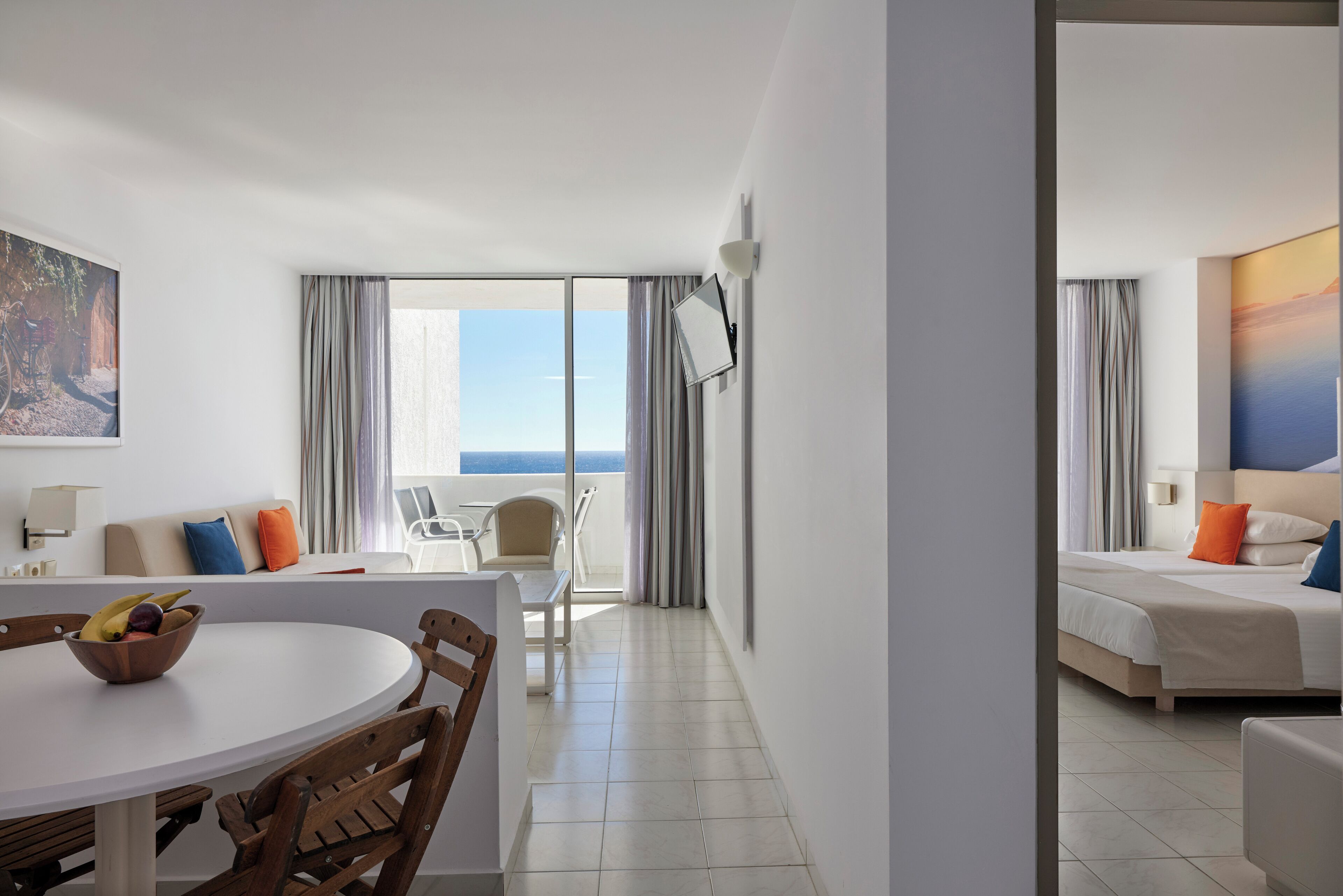 Een hotelkamer met balkon, een zithoek met tafel en stoelen, en een bed met kussens.