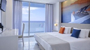 A hotel room with a large bed, a balcony with a view, a desk with a chair, and a TV. - Epsilon Hotel Apartments (Rhodes)