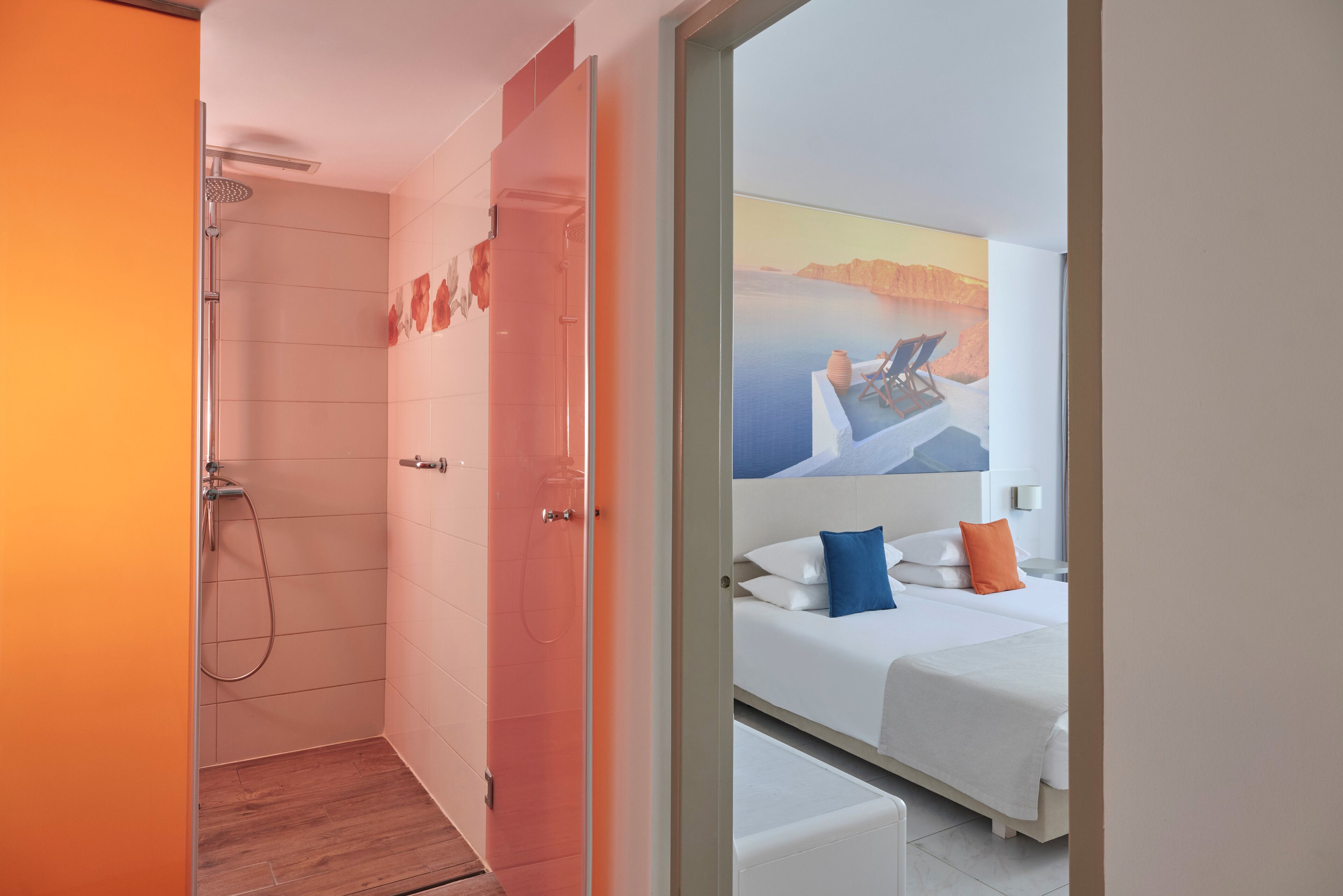 A modern hotel room with a shower, a bed with white bedding and colorful pillows, and a large window with a painting of a beach scene.