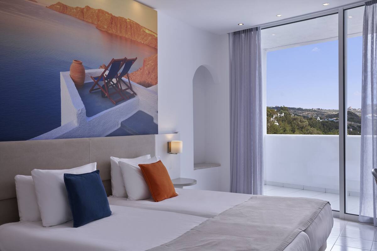 A modern hotel room with a large bed, two pillows, a nightstand, and a painting of a beach scene.
