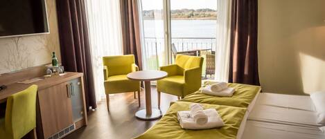 Habitación de hotel con cama, escritorio, silla, mesita y vista al agua.