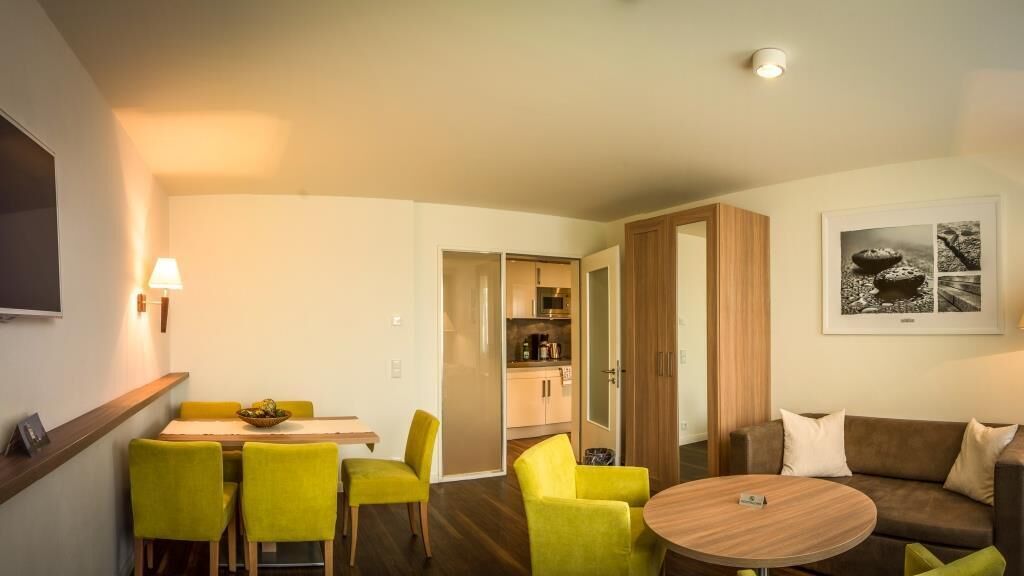 A modern living room with a dining area, a sofa, a coffee table, and a kitchen visible through an open door.