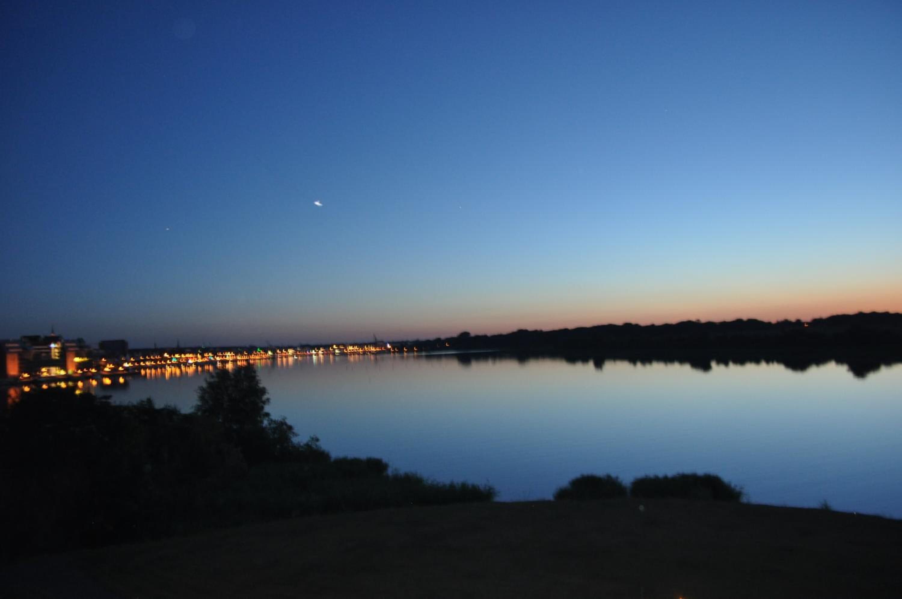 Een rustig meer bij zonsondergang, met lichtjes van de stad die in het water reflecteren.