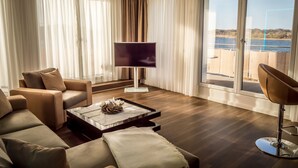 Un salón moderno con un sofá, una mesa de centro, un televisor y vistas a una masa de agua a través de amplias ventanas.