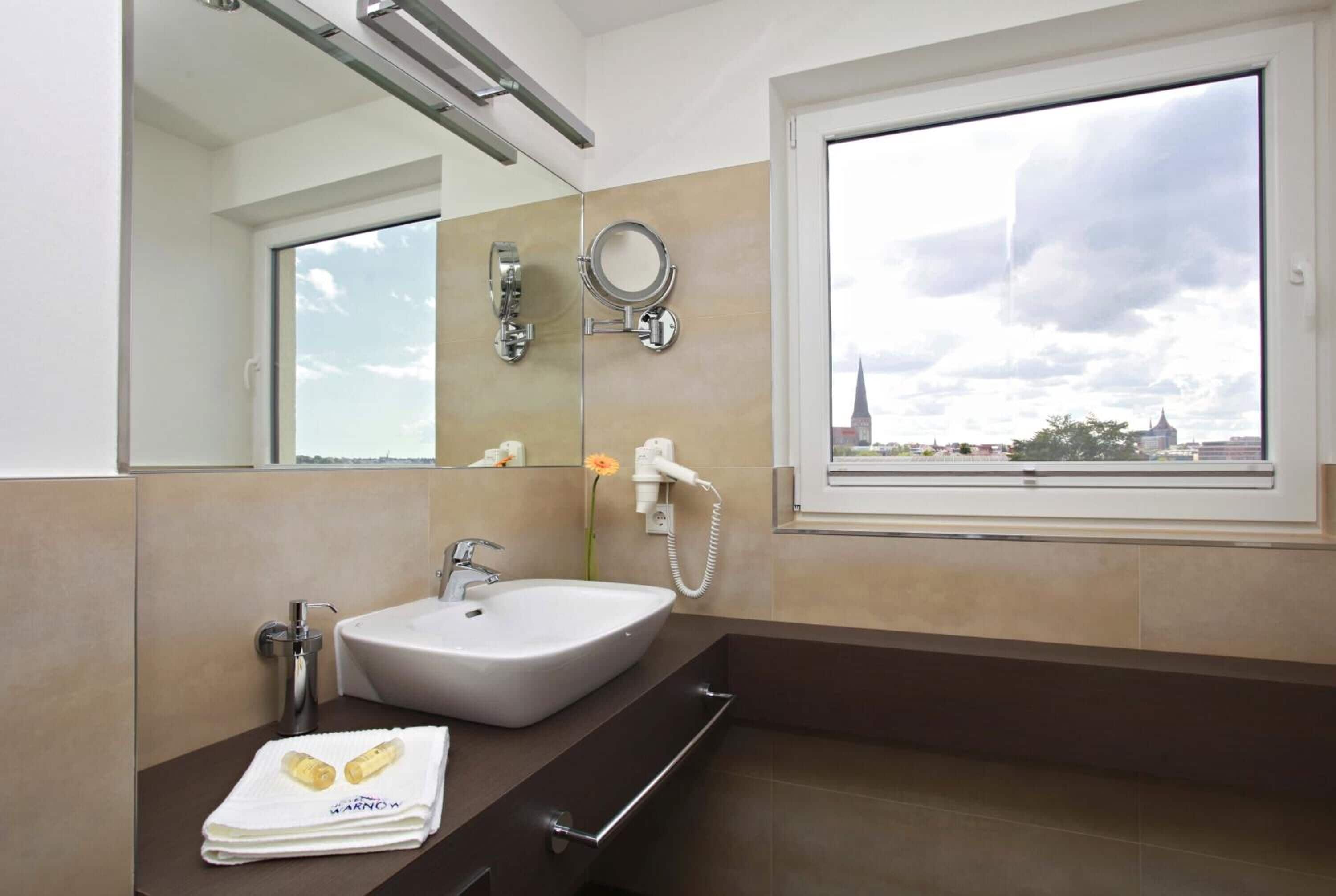 Ein modernes Badezimmer mit großem Fenster, Waschbecken, Spiegel und Handtuchhalter.