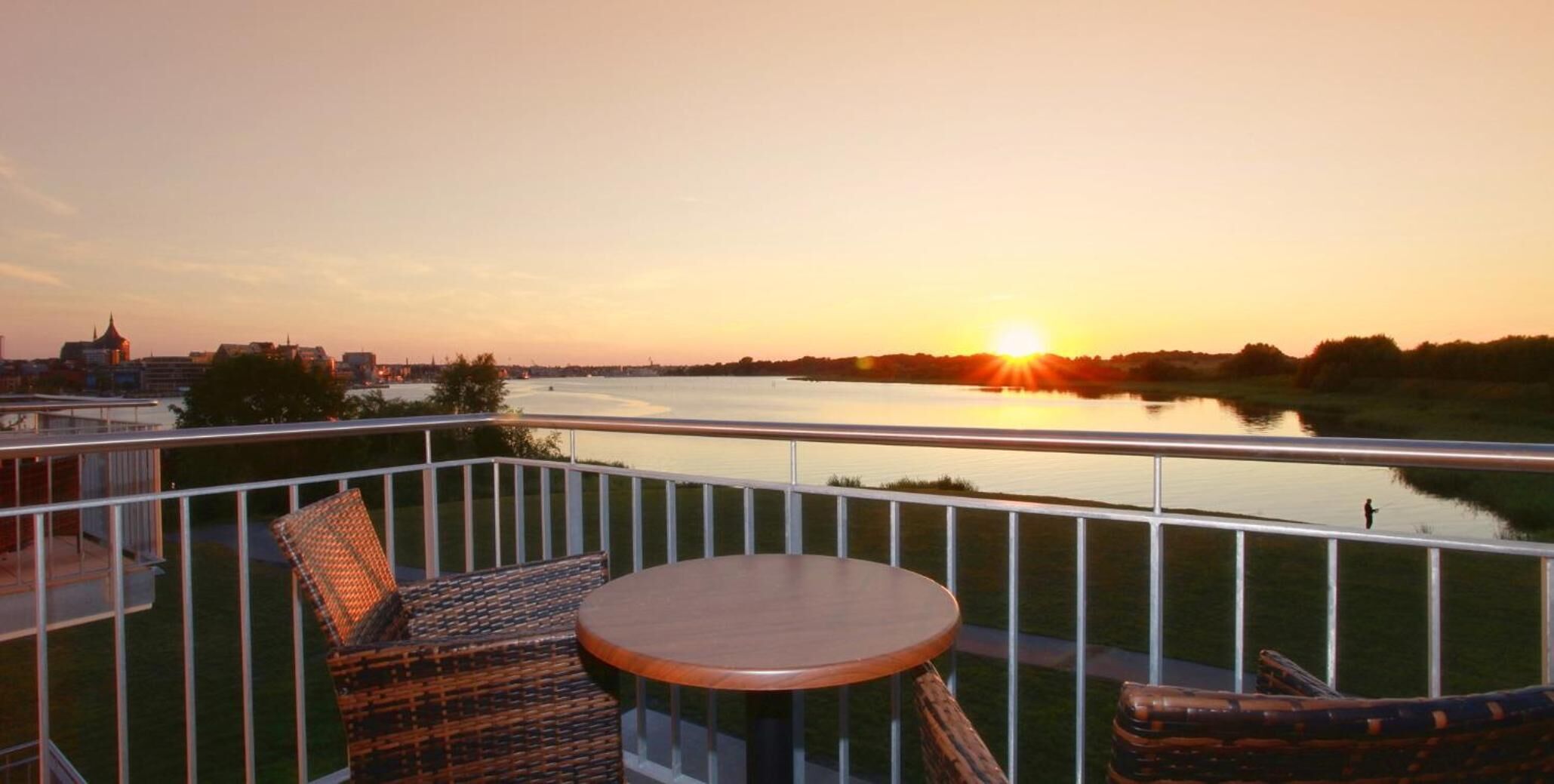 Ein Balkon mit Korbmöbeln und Blick auf einen Fluss bei Sonnenuntergang.