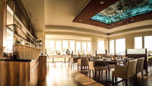 Un comedor espacioso con techo alto y ventanas amplias, que presenta un diseño moderno con una mesa central y sillas.