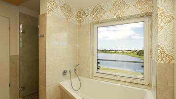 A bathroom with a bathtub, a shower, and a window with a view of a lake.