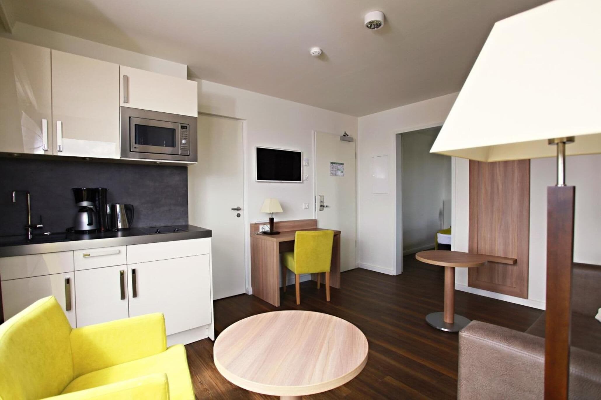 Una cocina compacta con microondas, cafetera y un pequeño comedor con una silla y una mesa.
