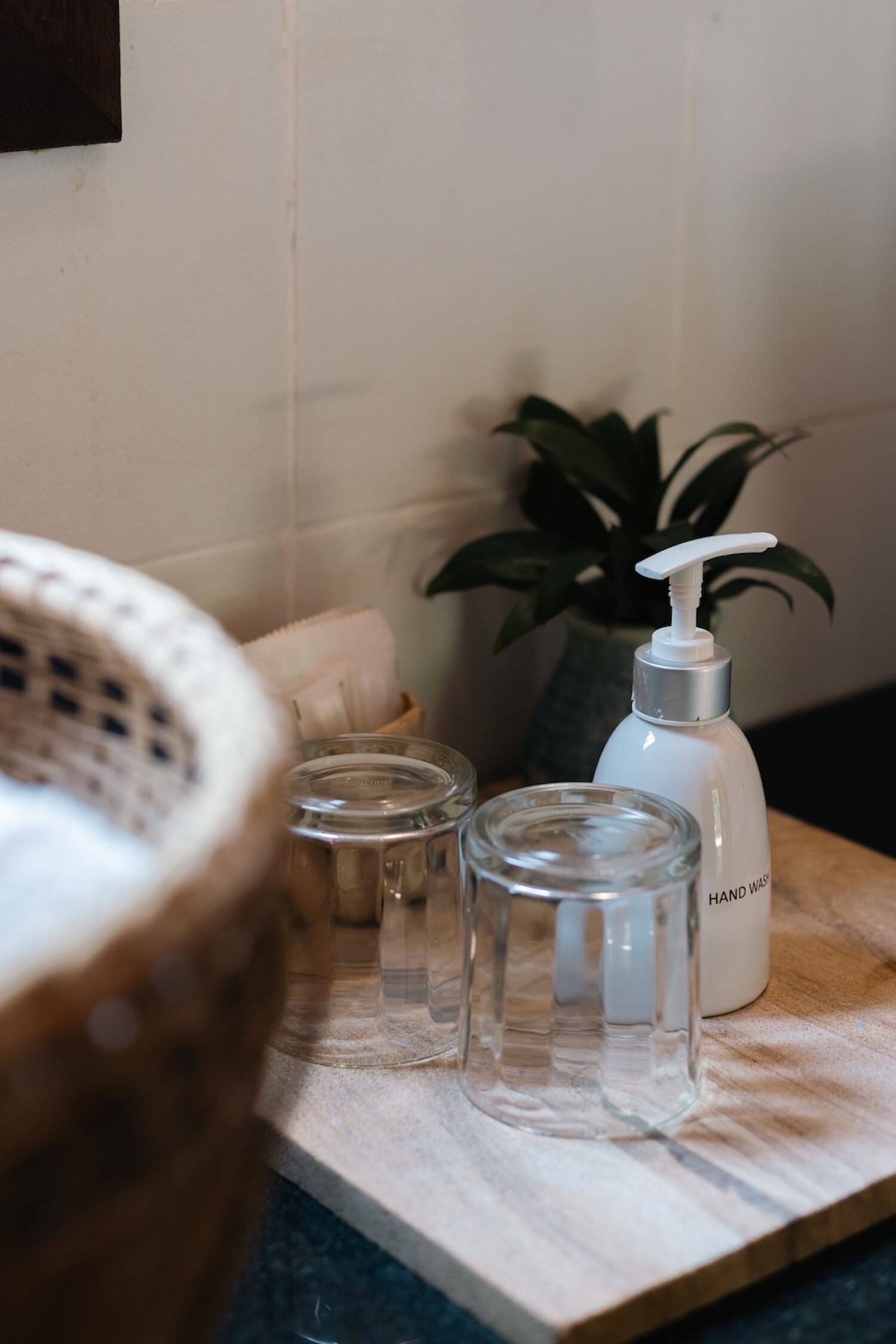 Uma bancada de banheiro com um dosador de sabonete líquido, um recipiente de vidro e uma bandeja de madeira.