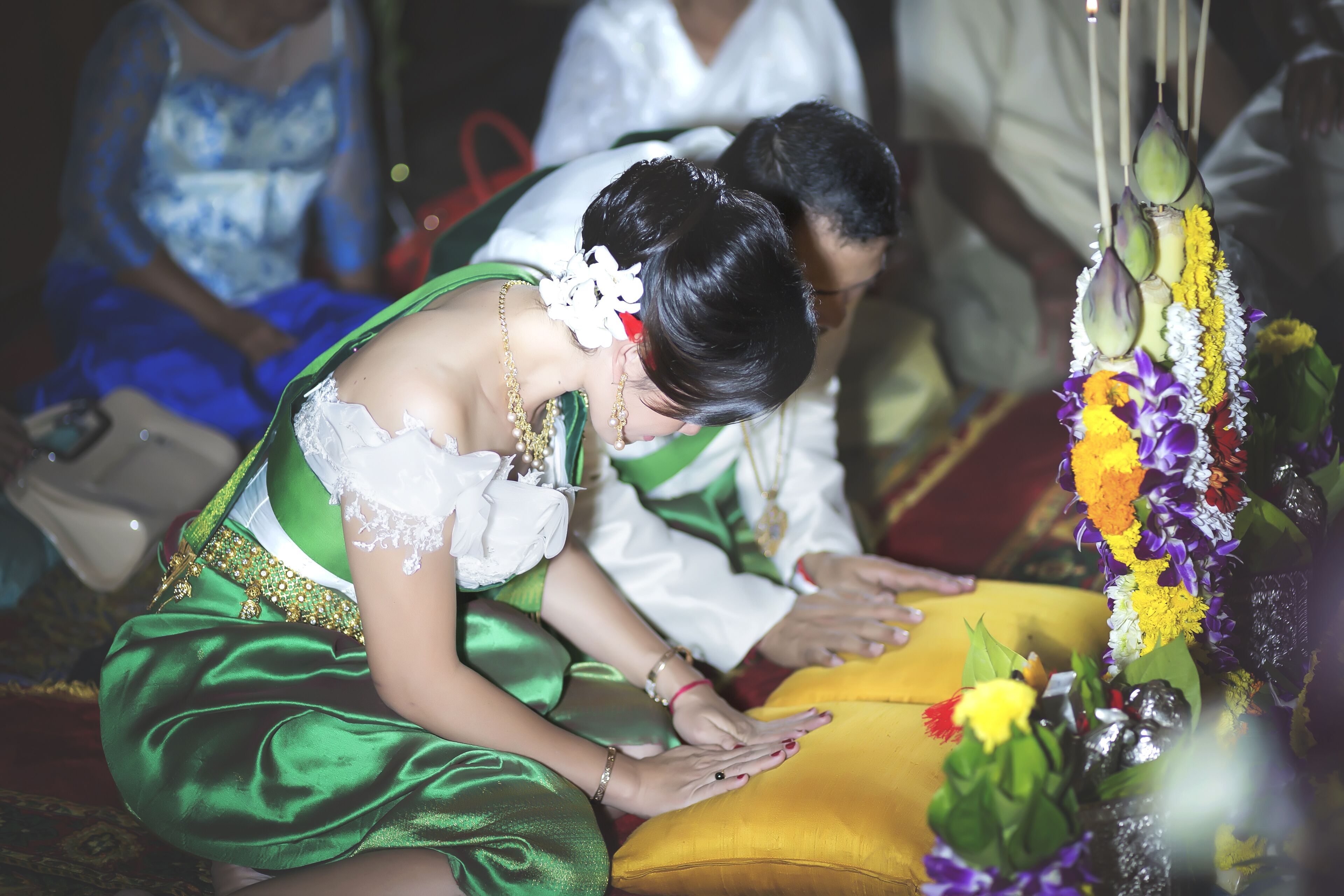 A person in a green dress with gold jewelry, sitting on a yellow cushion.