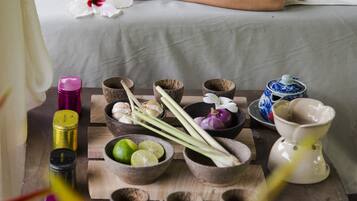 Un ambiente de spa con una persona descansando en una cama, rodeada de diversos cuencos y recipientes con hierbas y flores.