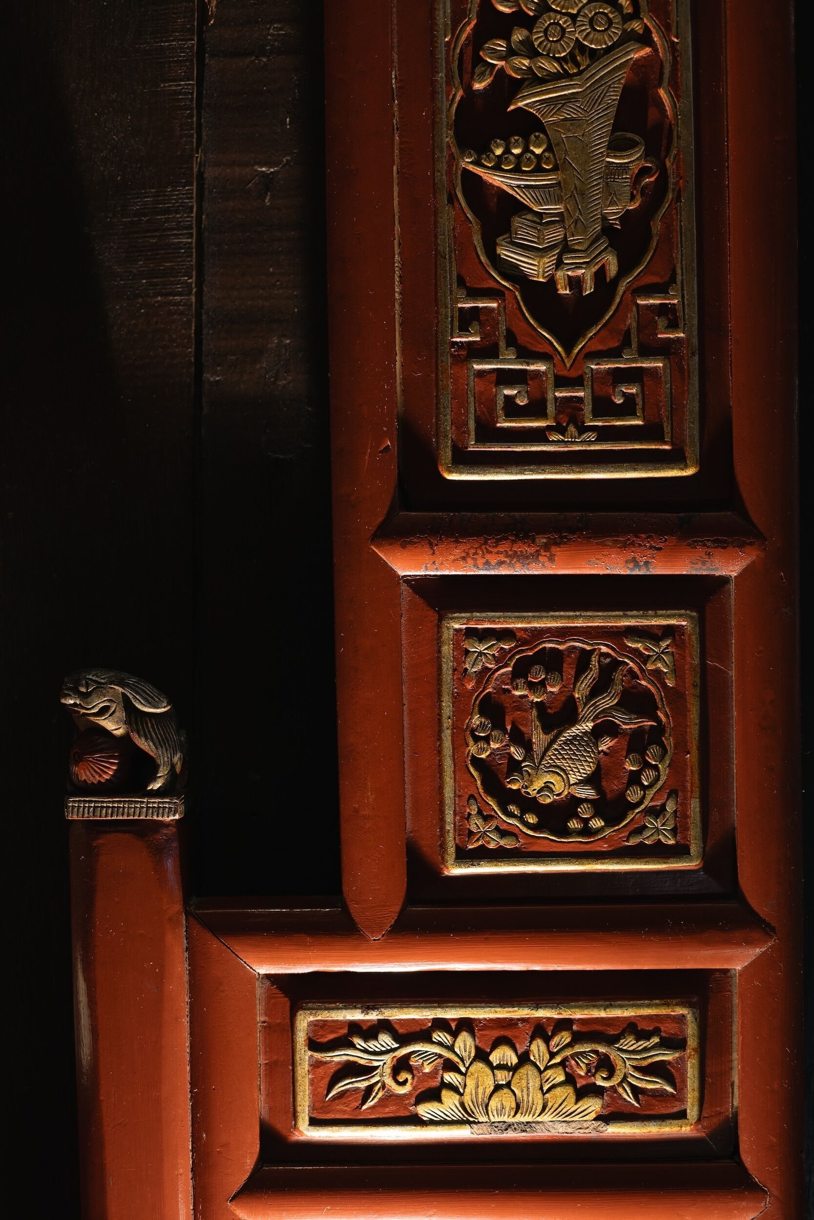 A wooden door with intricate carvings, including a lion head, a fish, and floral designs.