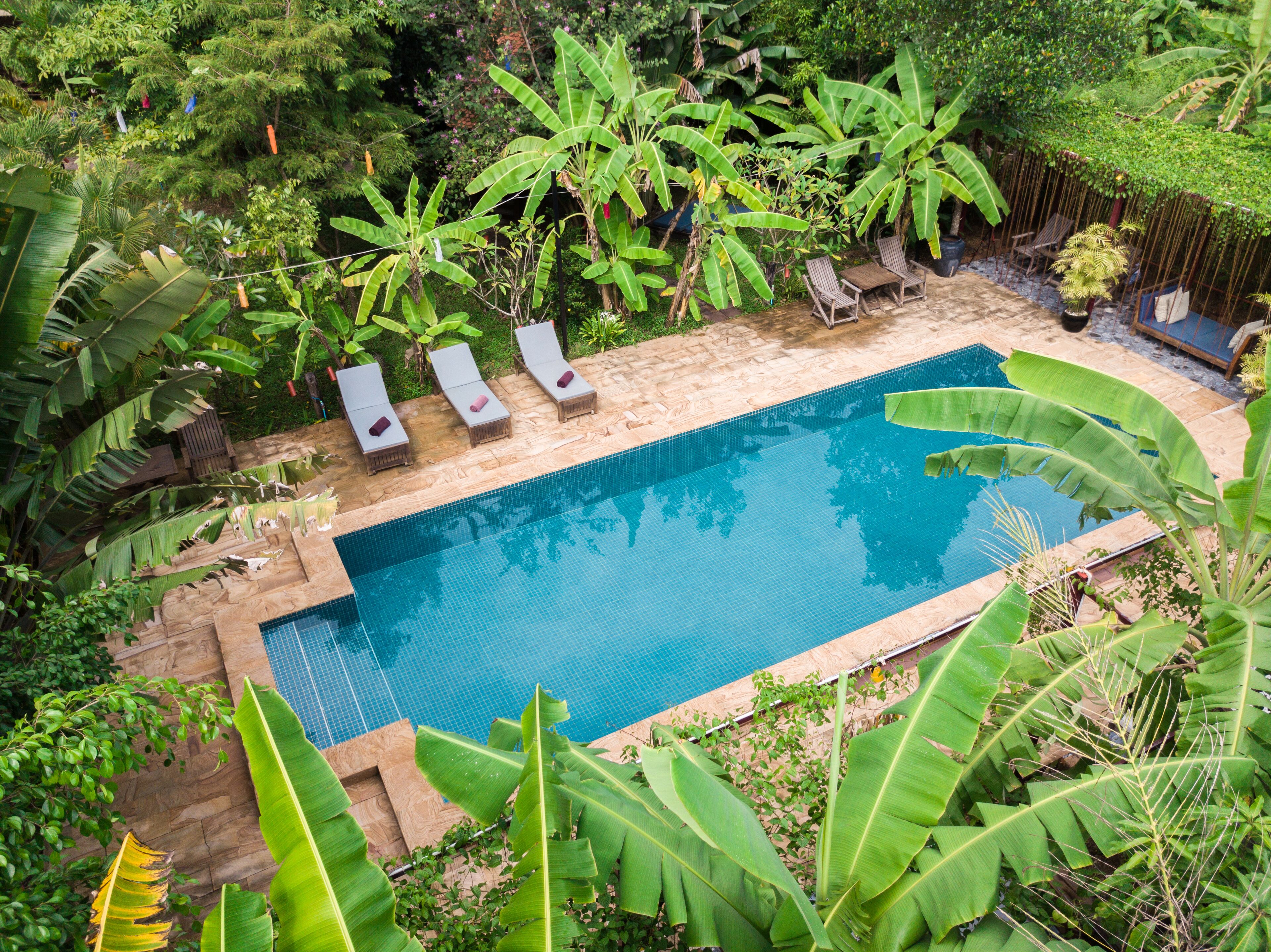 Piscina rectangular con tres sillas de descanso y una terraza de madera alrededor.