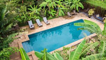 Piscina rectangular con tres sillas de descanso y una terraza de madera alrededor.
