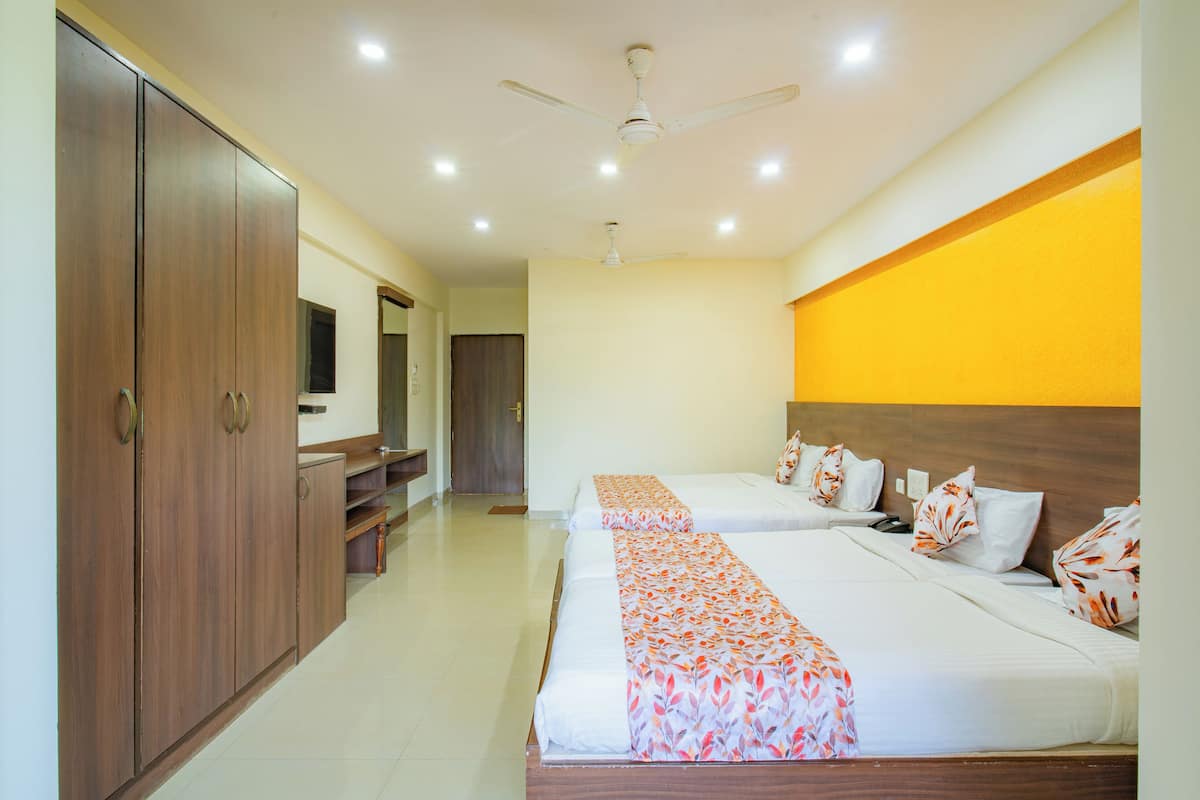 A hotel room with two beds, a wardrobe, a desk, and a television.