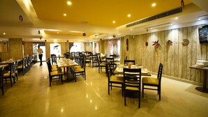 A spacious restaurant with multiple dining tables and chairs, wooden panel walls, and ceiling lights.