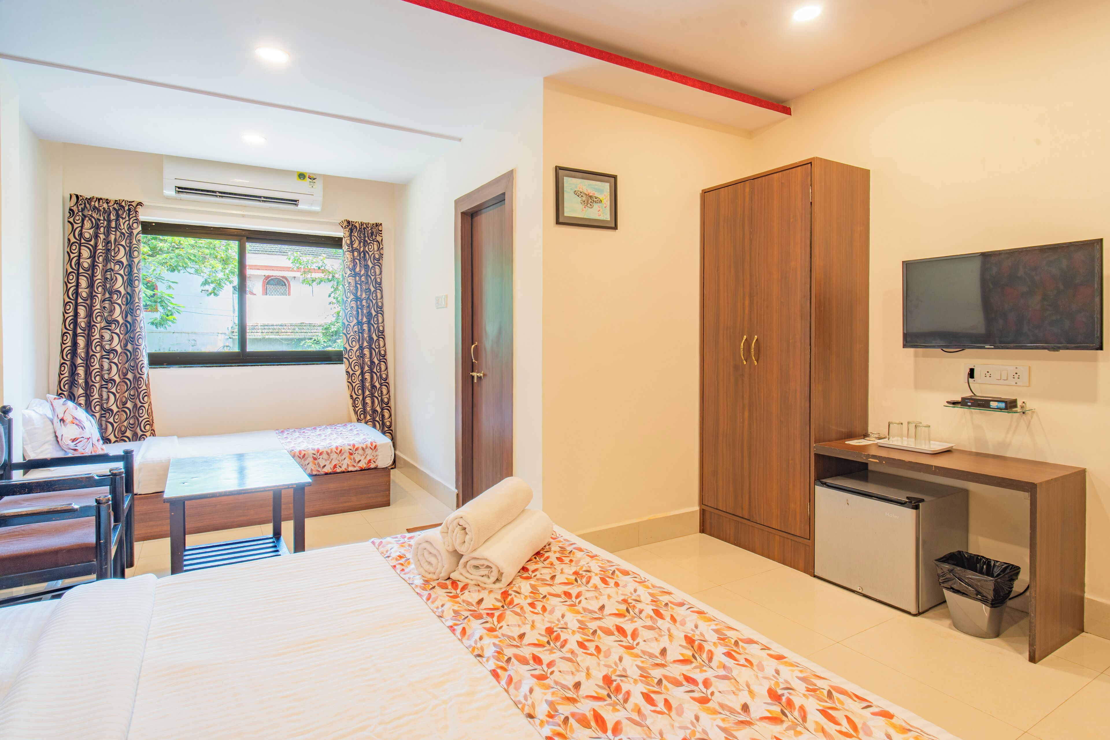 A hotel room with a bed, a desk with a television, a small fridge, and a window with curtains.