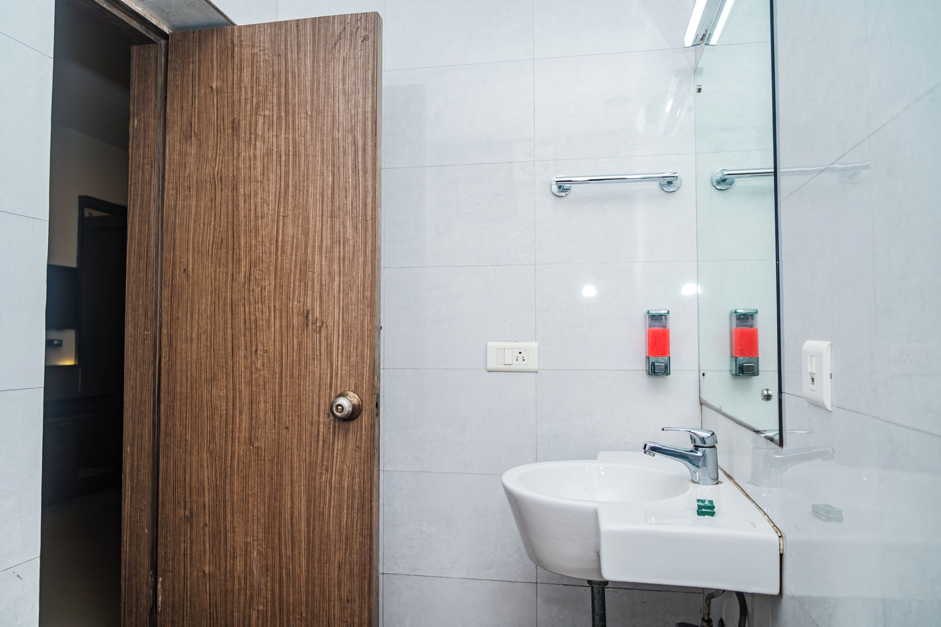 Un baño con puerta de madera, azulejos blancos, un lavabo y un espejo.
