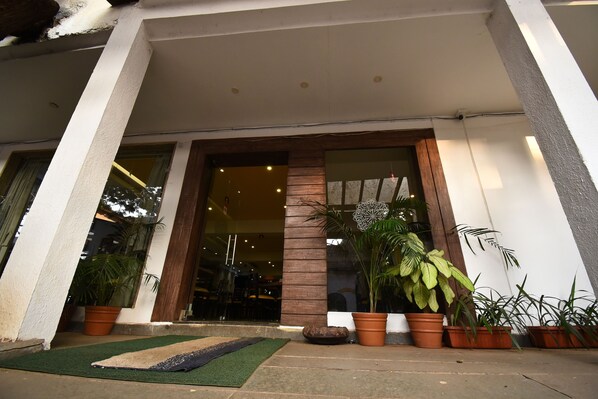A hotel entrance with a glass door, potted plants, and a small outdoor seating area.