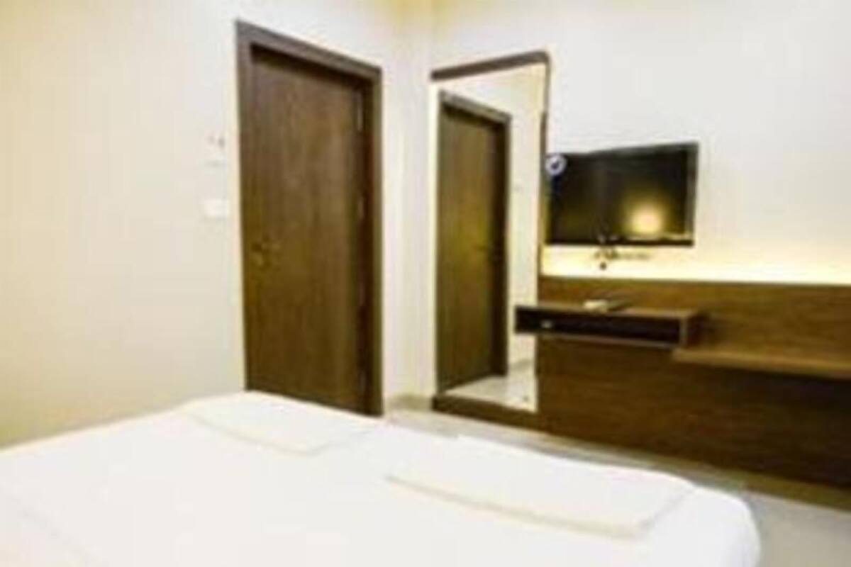 A hotel room with a bed, a wooden headboard, a bedside table, and a wall-mounted TV.
