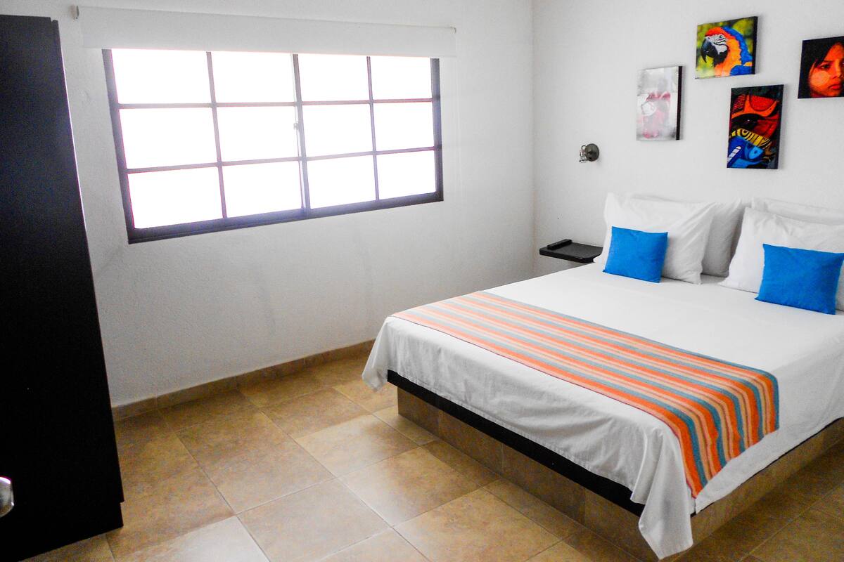 Habitación de hotel con cama, mesita de noche, ventana y una pared decorada con obras de arte.