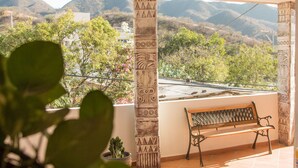 Ein Balkon mit einer Holzbank, einer Zierpfeiler und Blick auf eine gebirgige Landschaft.