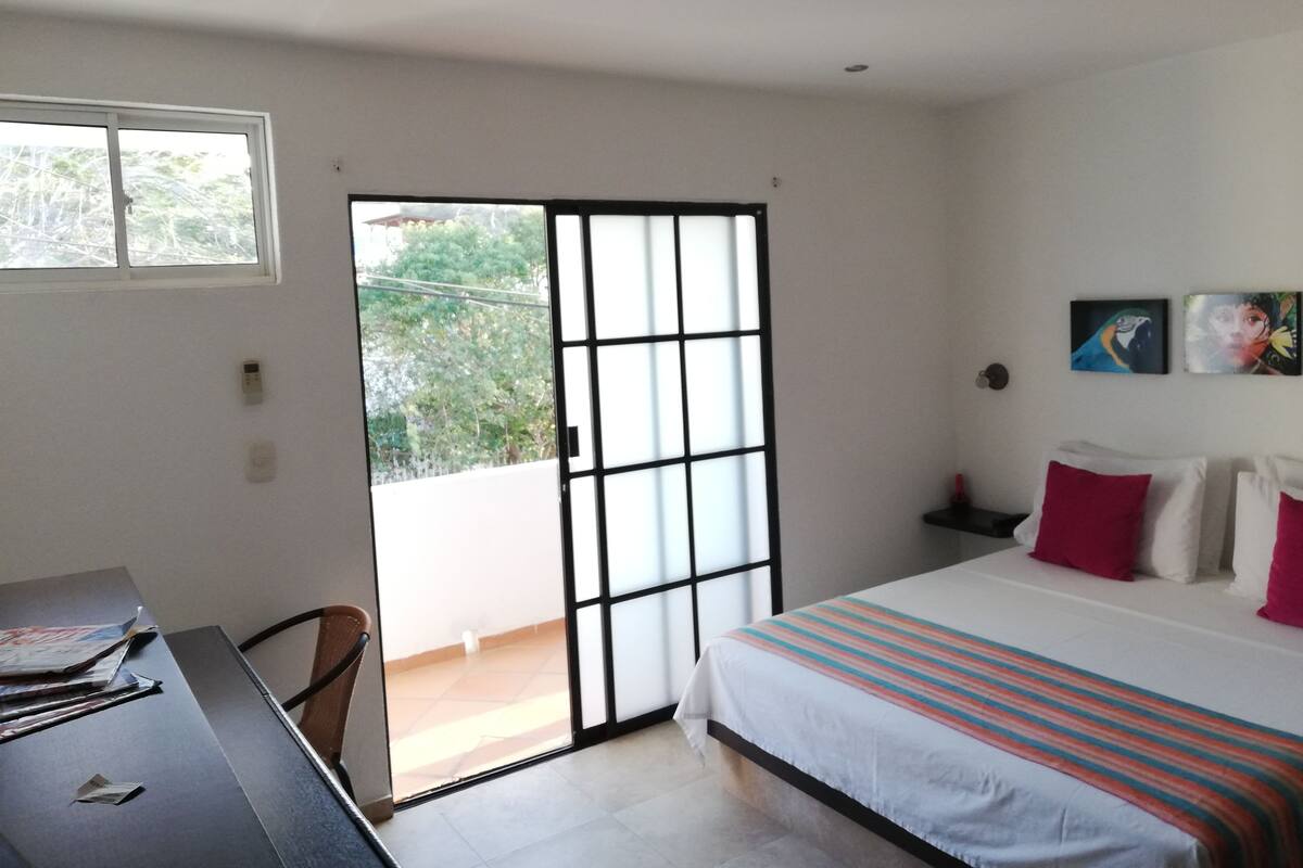 Un dormitorio con cama, escritorio, silla, puerta corrediza de vidrio y dos cuadros colgados en la pared.