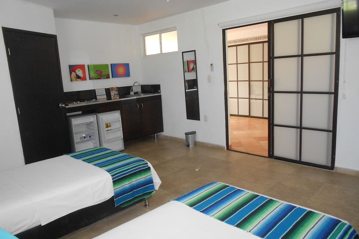 Un dormitorio con dos camas, una kitchenette pequeña, una puerta corrediza y un ventanal.