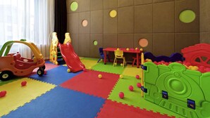 Un área de juegos infantiles con colchonetas de espuma, estructuras de juego y una mesa con sillas.