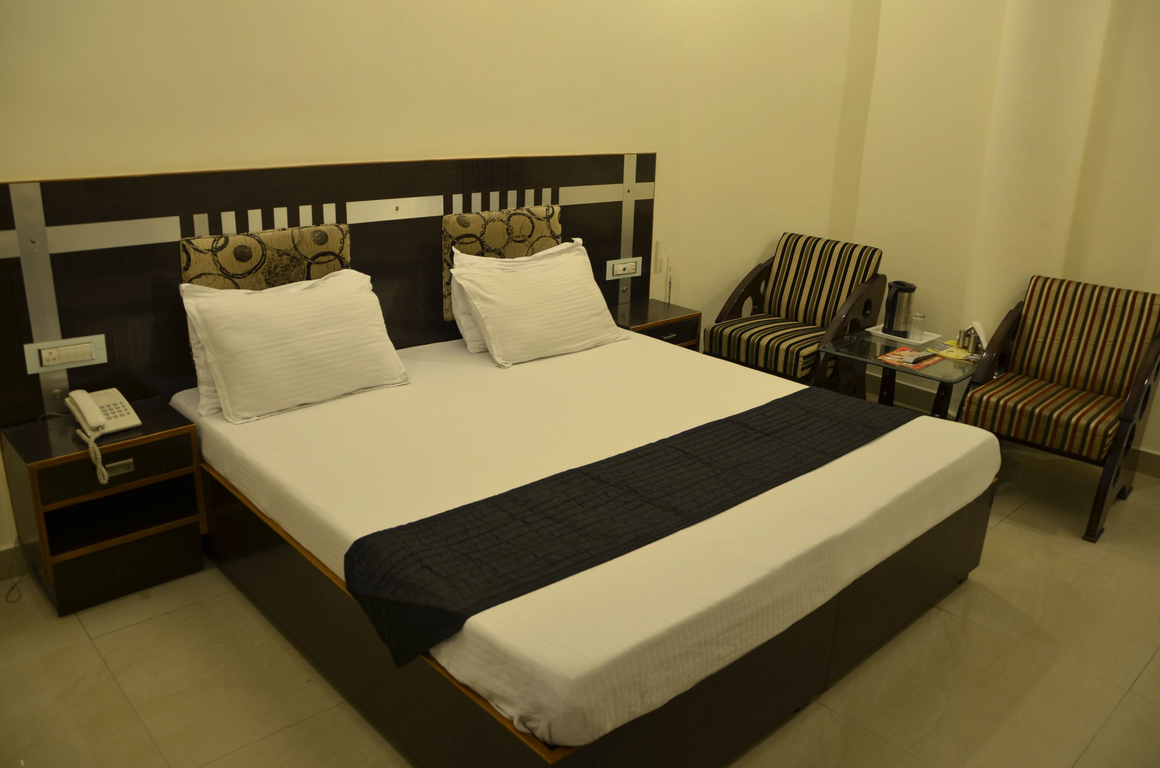 A hotel room with a large bed, two nightstands, a chair, and a small table with a lamp.