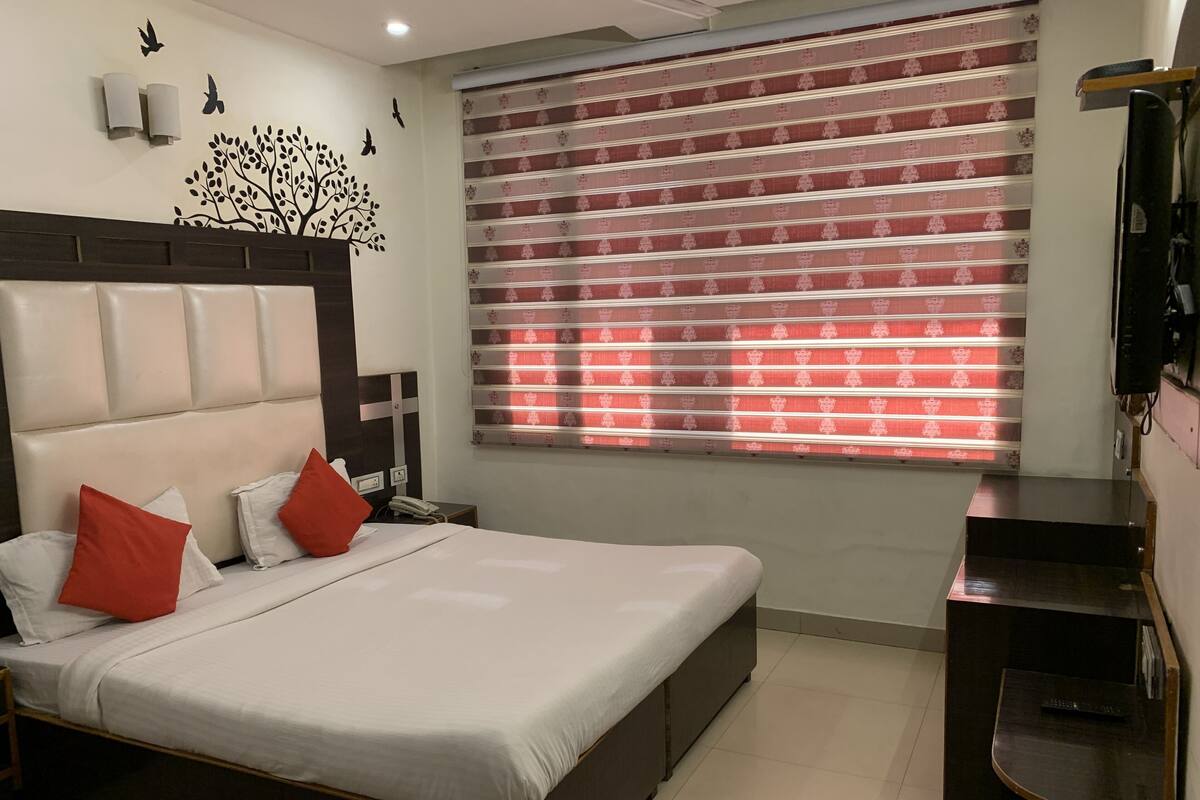 A neatly arranged bedroom with a bed, pillows, a bedside table, a telephone, and a window with patterned curtains.