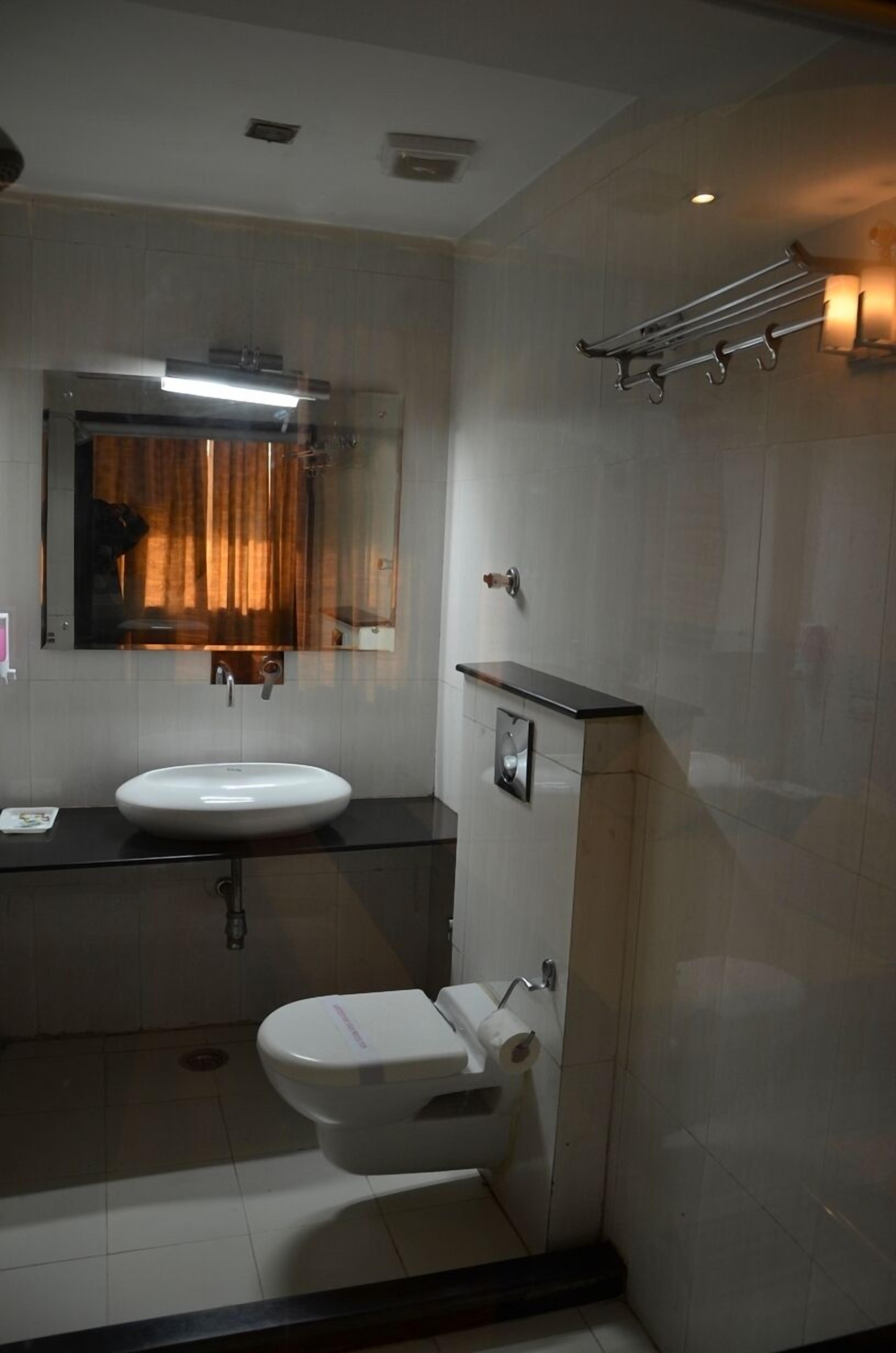Un baño moderno con lavamanos, espejo y retrete blancos. Hay un perchero sobre el lavamanos y una ducha en la pared.