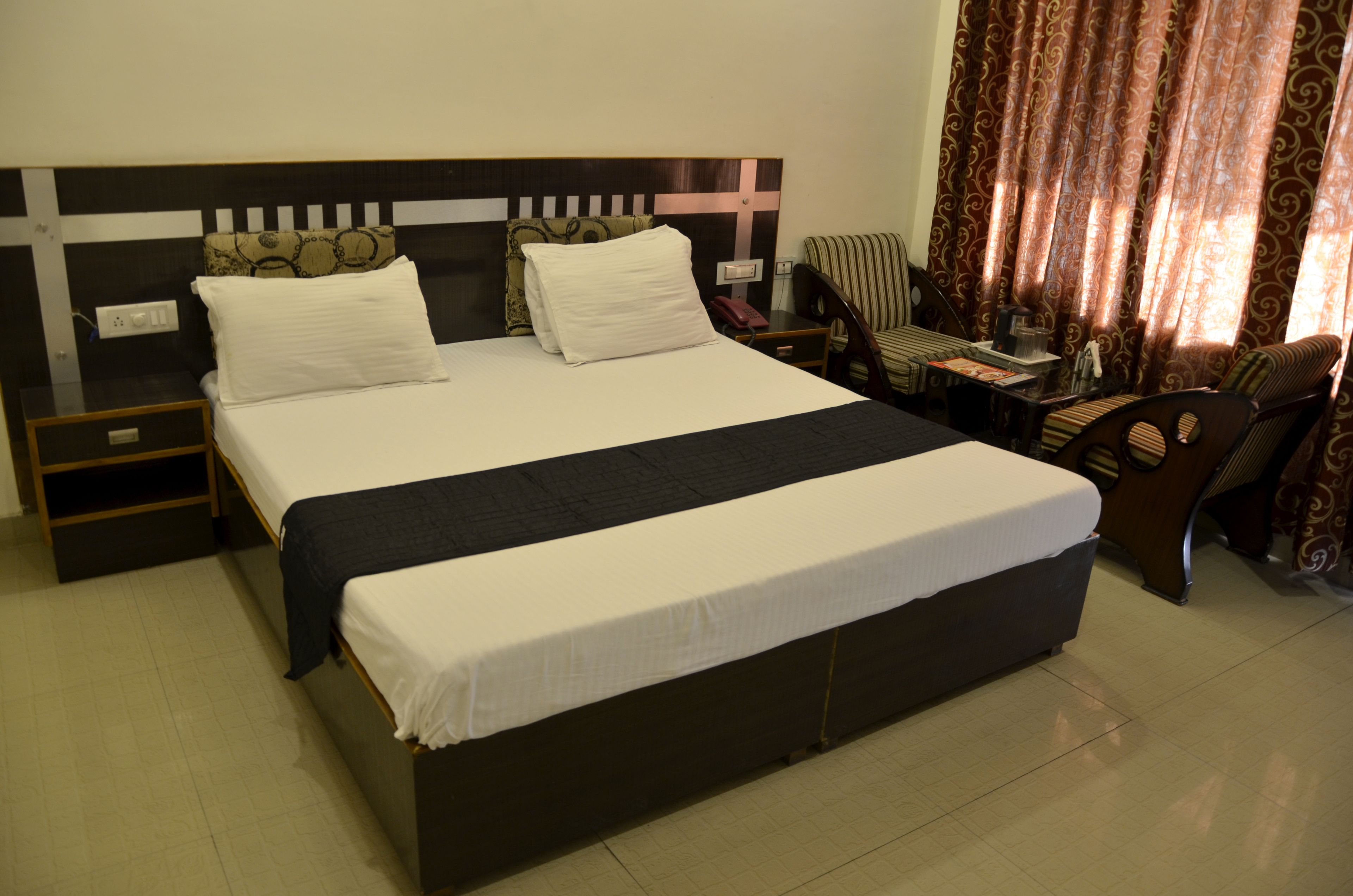 A neatly made bed with white linens, a wooden headboard with a cross design, and a brown chair with a striped cushion.