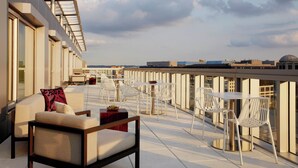 Una terraza en la azotea con mobiliario exterior, amplias ventanas y vistas del horizonte urbano.