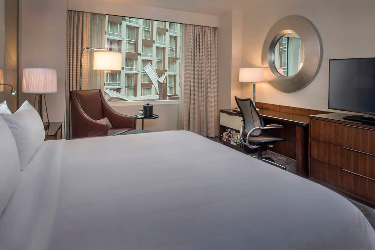 A hotel room with a large bed, two chairs, a desk, a television, and a window with curtains.