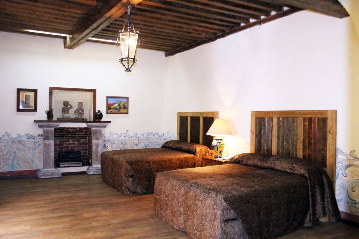 A room with two beds, a fireplace, and a wooden ceiling.