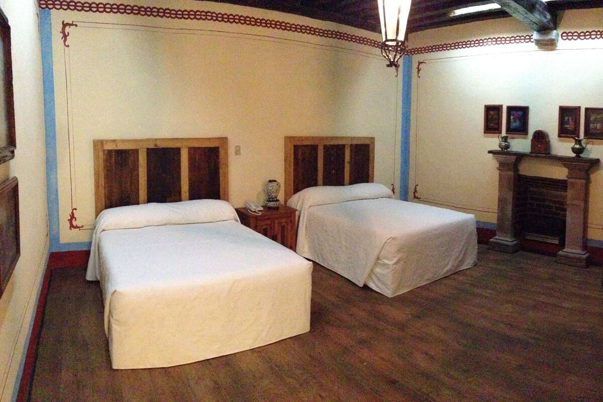 A room with two beds, wooden flooring, a fireplace, and a decorative border on the walls.