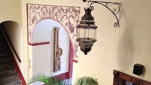 A staircase with a potted plant, a decorative wall with an ornate arch, and a wall-mounted lantern. - Hotel Casa de la Palma Travel (Puebla)