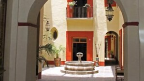 An arched corridor with a fountain, a balcony, and a hanging light fixture. - Hotel Casa de la Palma Travel (Puebla)