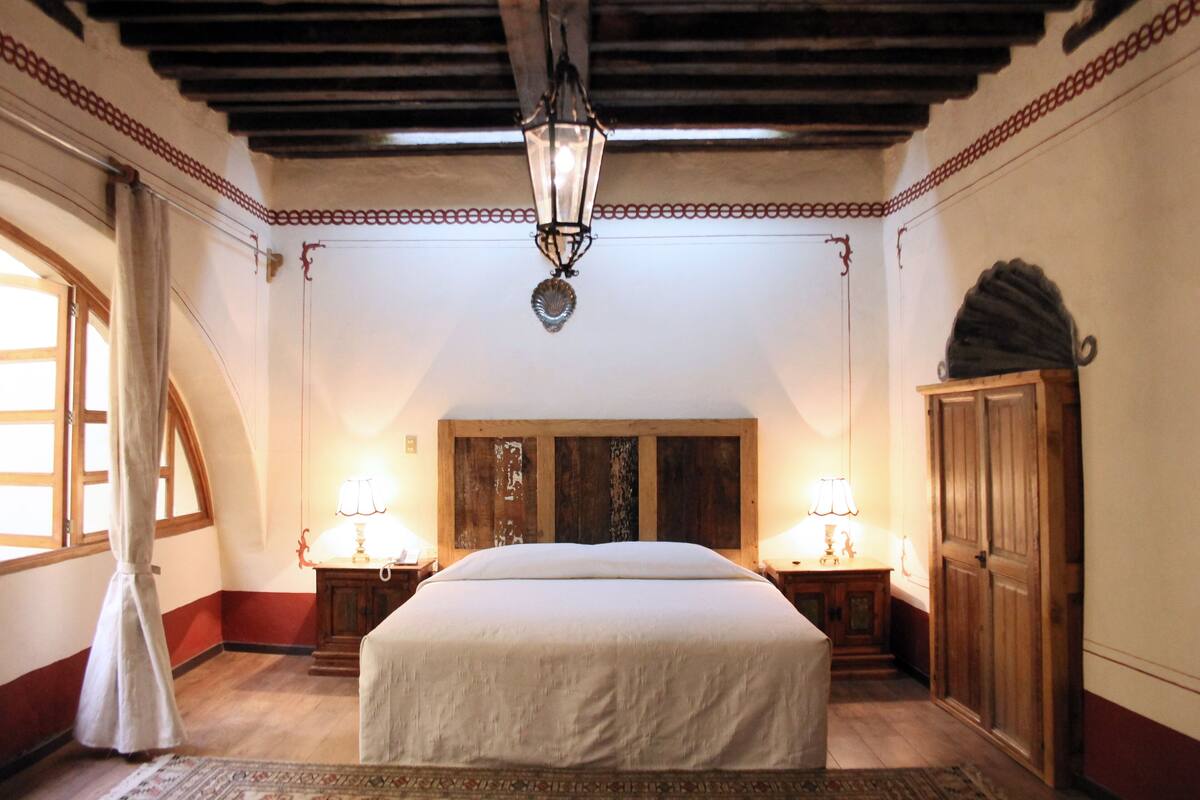 A bedroom with a large bed, wooden headboard, two bedside tables with lamps, a wardrobe, and a decorative ceiling light.